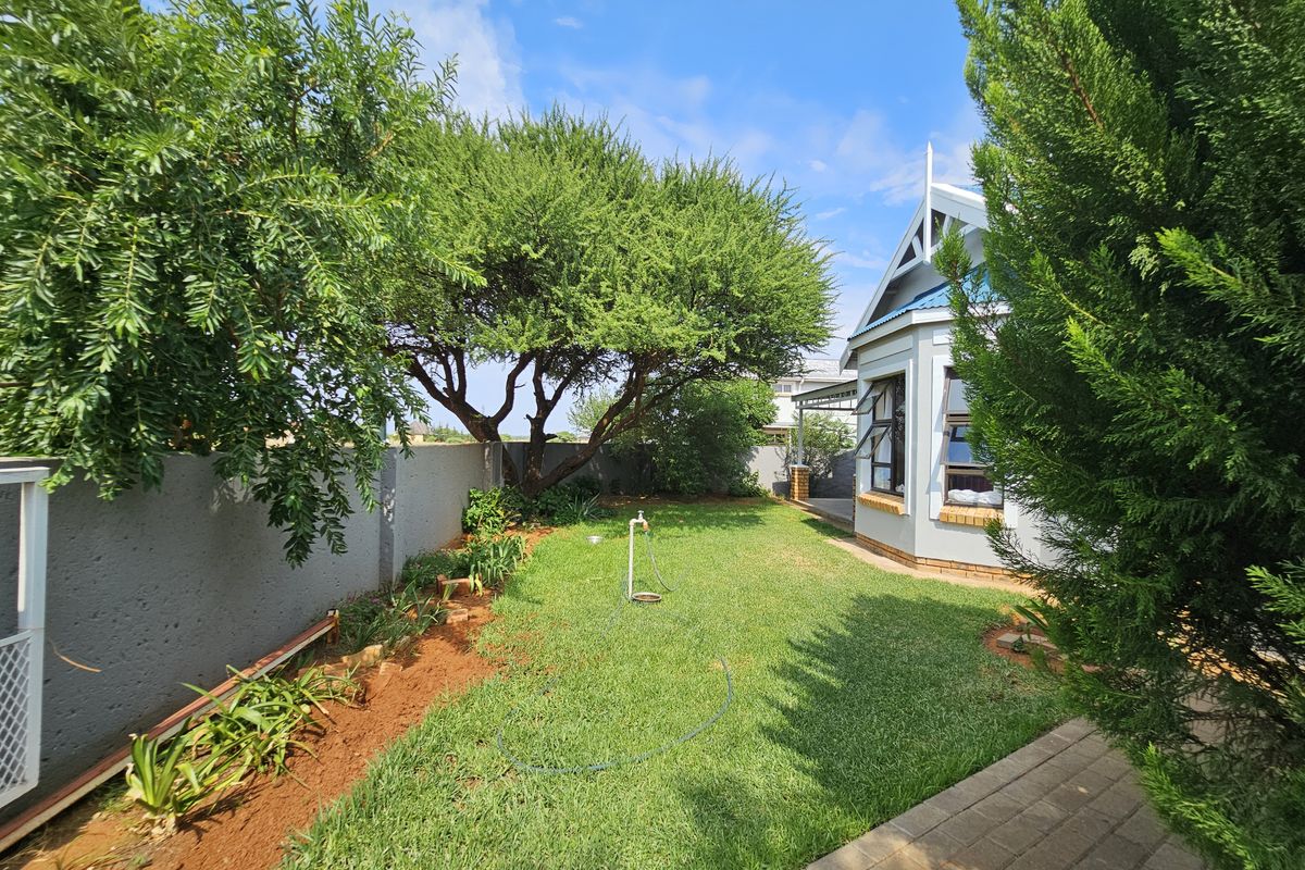 A well-maintained rear garden featuring a lush lawn, boundary wall, and paved walkway adjacent to the side of the house.