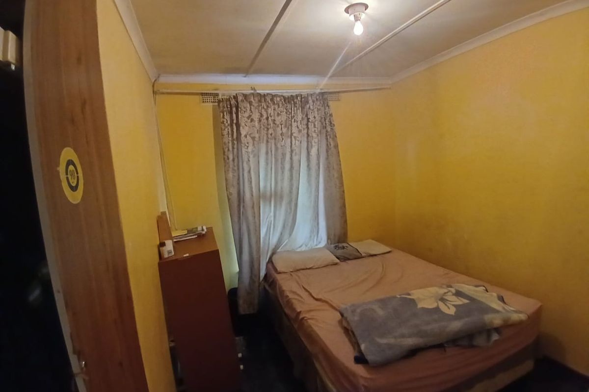 A compact bedroom featuring yellow walls, a central ceiling light fixture, and a window with curtain track.