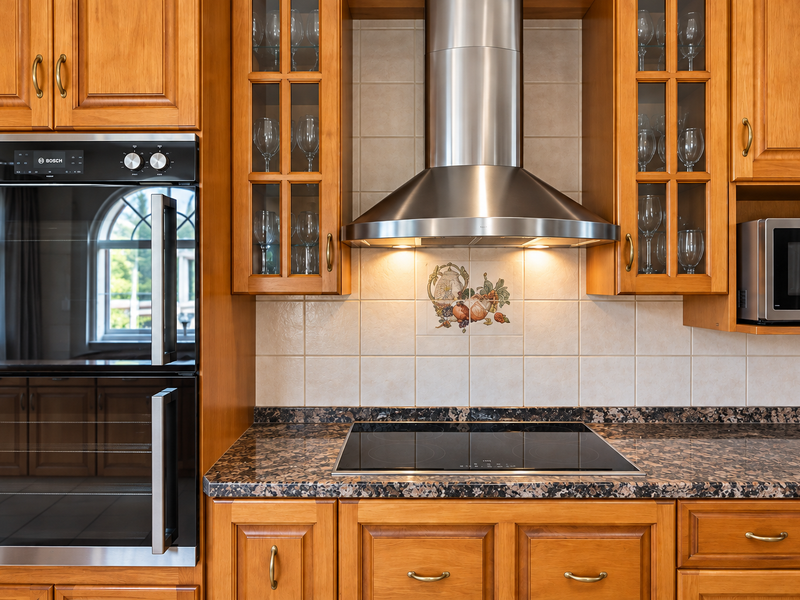 A well-maintained kitchen featuring warm wood cabinetry, granite countertops, a built-in Bosch oven, induction cooktop, and a stainless steel extractor fan.