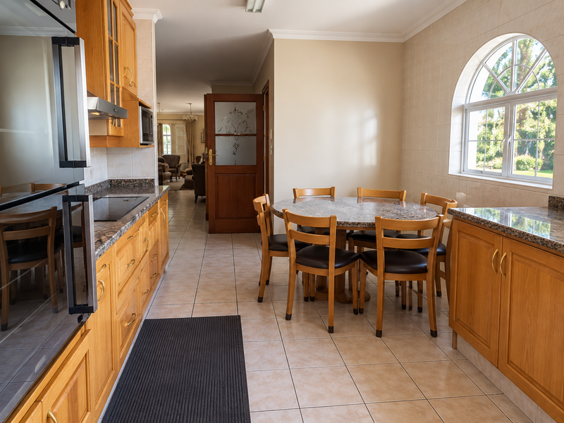 A functional kitchen featuring wooden cabinetry, granite countertops, built-in appliances, and tiled flooring, with an adjacent dining area and arched window.