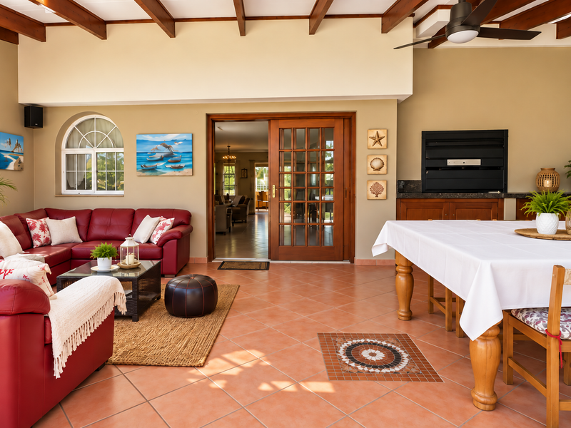 Spacious covered patio featuring exposed timber beams, terracotta flooring with mosaic detail, a built-in braai, and direct access to the interior living area.