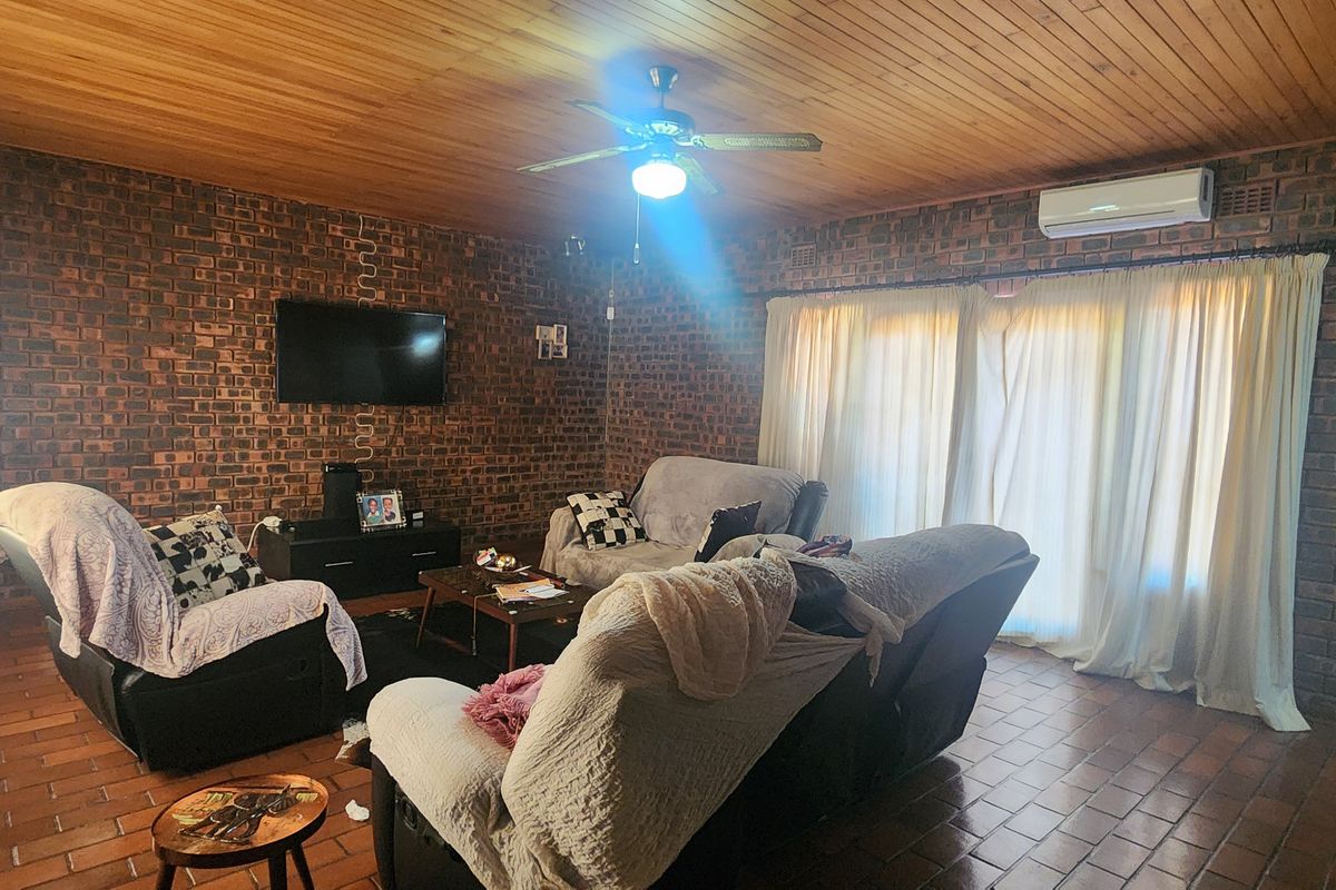 Spacious living room featuring rustic exposed brick walls, a warm timber ceiling, tiled flooring, and integrated climate control via a split-system air conditioner.