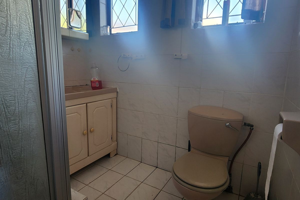 A functional bathroom featuring a vanity cabinet, basin, toilet, and shower enclosure with tiled finishes and leaded glass windows.