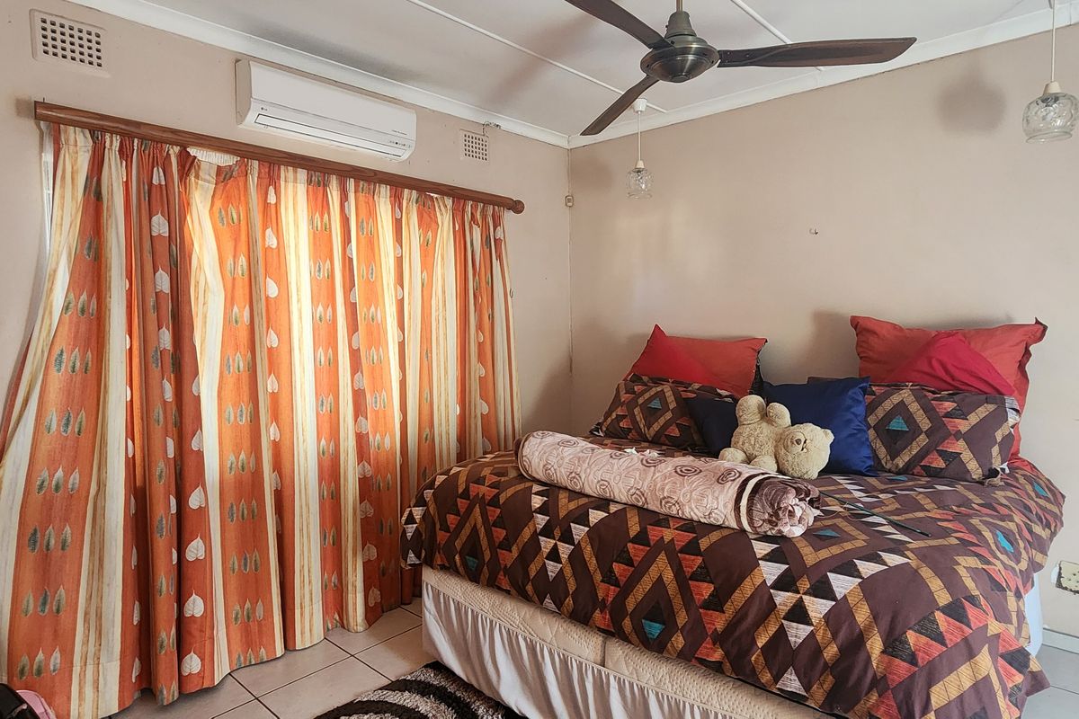 A functional bedroom featuring tiled flooring, a ceiling fan, and a wall-mounted split-system air conditioning unit.