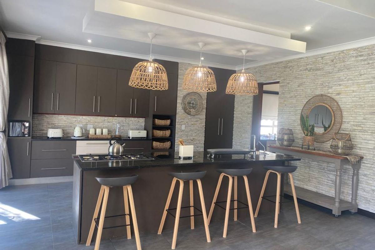 Modern kitchen featuring dark cabinetry, a central island with a gas hob, and a textured stone feature wall with recessed ceiling lighting.