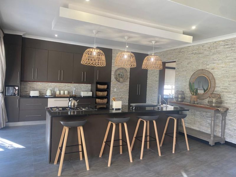 Modern kitchen featuring dark cabinetry, a central island with a gas hob, and a textured stone feature wall with recessed ceiling lighting.