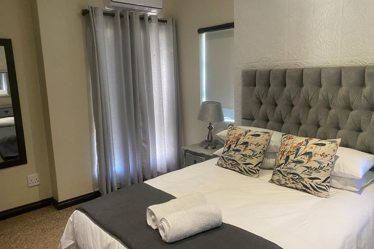 A well-maintained bedroom featuring a textured accent wall, carpeted flooring, and a wall-mounted split-system air conditioning unit.