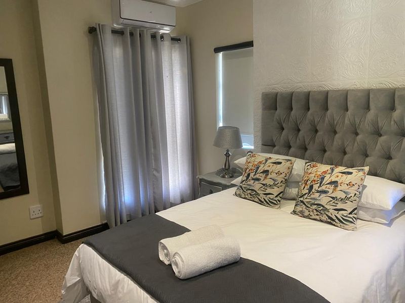 A well-maintained bedroom featuring a textured accent wall, carpeted flooring, and a wall-mounted split-system air conditioning unit.