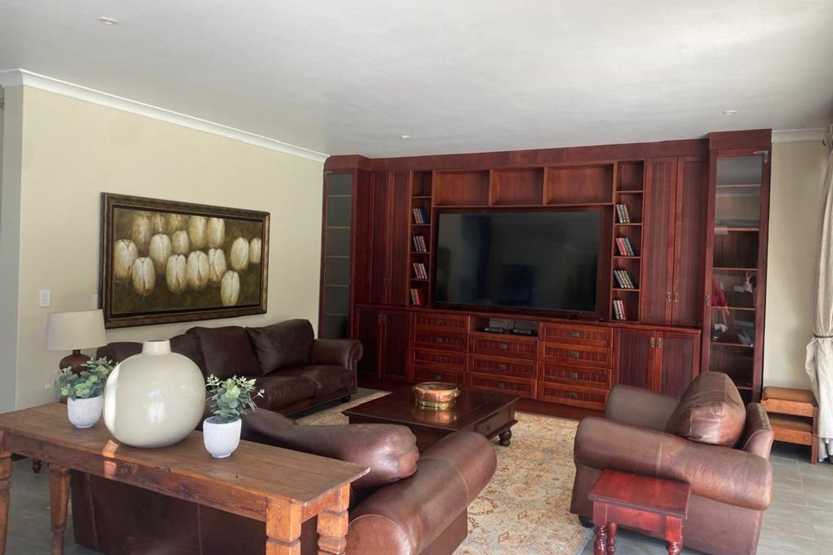 A spacious living room featuring extensive built-in wooden cabinetry and shelving, tiled flooring, and recessed ceiling lighting.