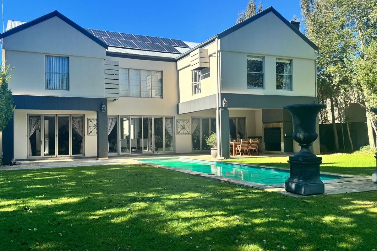 Rear view of a two-story house featuring a swimming pool, covered patio with built-in braai, and solar panels on the roof.