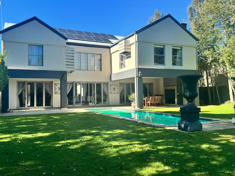 Rear view of a two-story house featuring a swimming pool, covered patio with built-in braai, and solar panels on the roof.