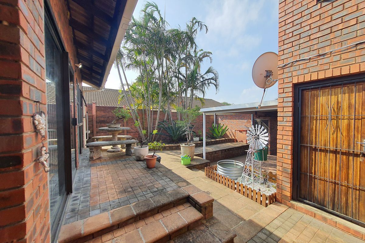 A private rear courtyard featuring brick paving, tiered garden beds, and direct access to the home through sliding glass doors.