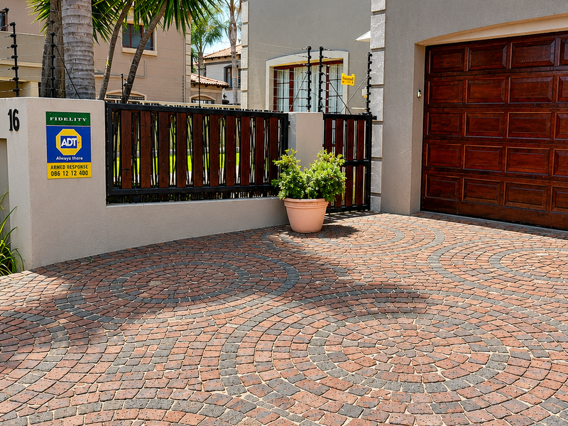 Front exterior view of the property featuring a patterned paved driveway, wooden garage door, and secure perimeter fencing with an electric security system.