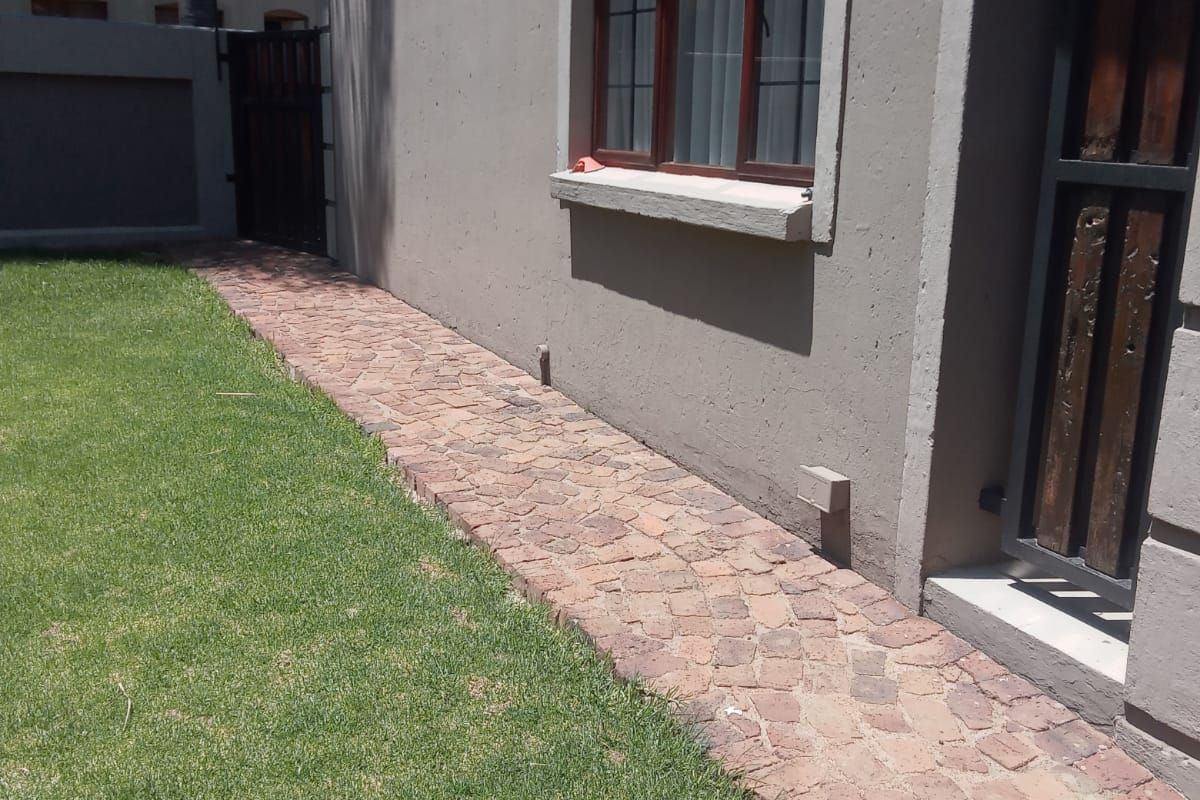 A well-maintained rear garden area featuring a neat cobblestone pathway, manicured lawn, and secure boundary walling.