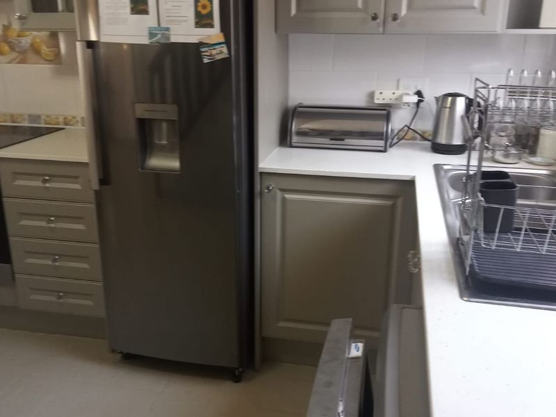 A functional kitchen featuring neutral-toned cabinetry, stone countertops, a stainless steel sink, and tiled flooring with a clean, practical layout.