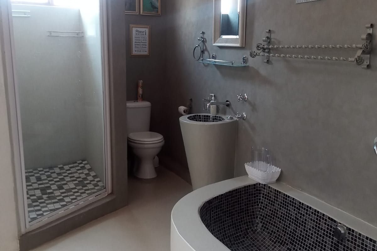 A modern bathroom featuring a built-in bathtub with mosaic tiling, a separate shower enclosure, a pedestal sink, and a toilet.
