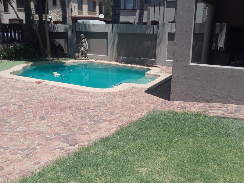A private backyard featuring a swimming pool, paved patio area, and a covered outdoor space, enclosed by a secure boundary wall.