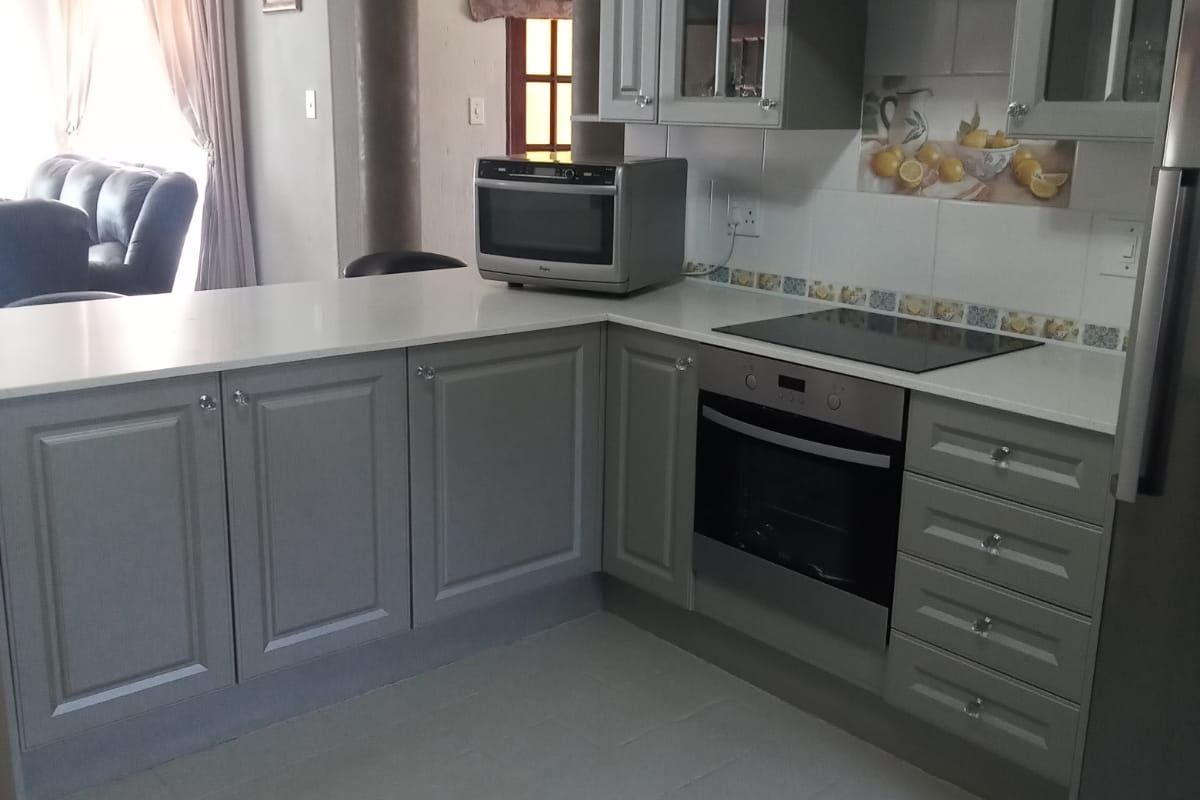 Modern kitchen featuring grey cabinetry, stone countertops, integrated electric hob, oven, and extractor fan, with a seamless transition to the adjacent living area.