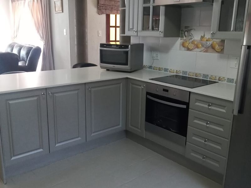 Modern kitchen featuring grey cabinetry, stone countertops, integrated electric hob, oven, and extractor fan, with a seamless transition to the adjacent living area.