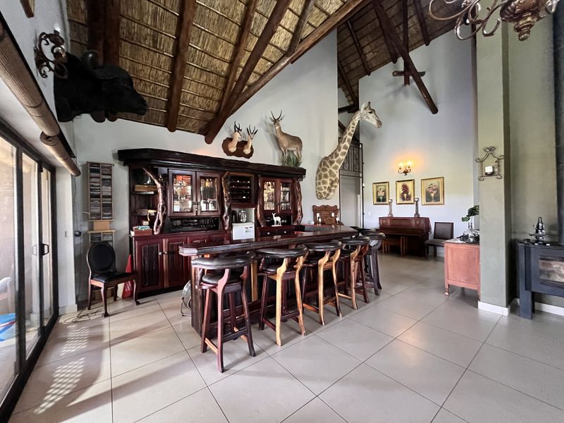 Spacious bar area featuring a custom built-in wooden bar, high vaulted thatched ceilings with exposed timber trusses, and large sliding doors leading outdoors.
