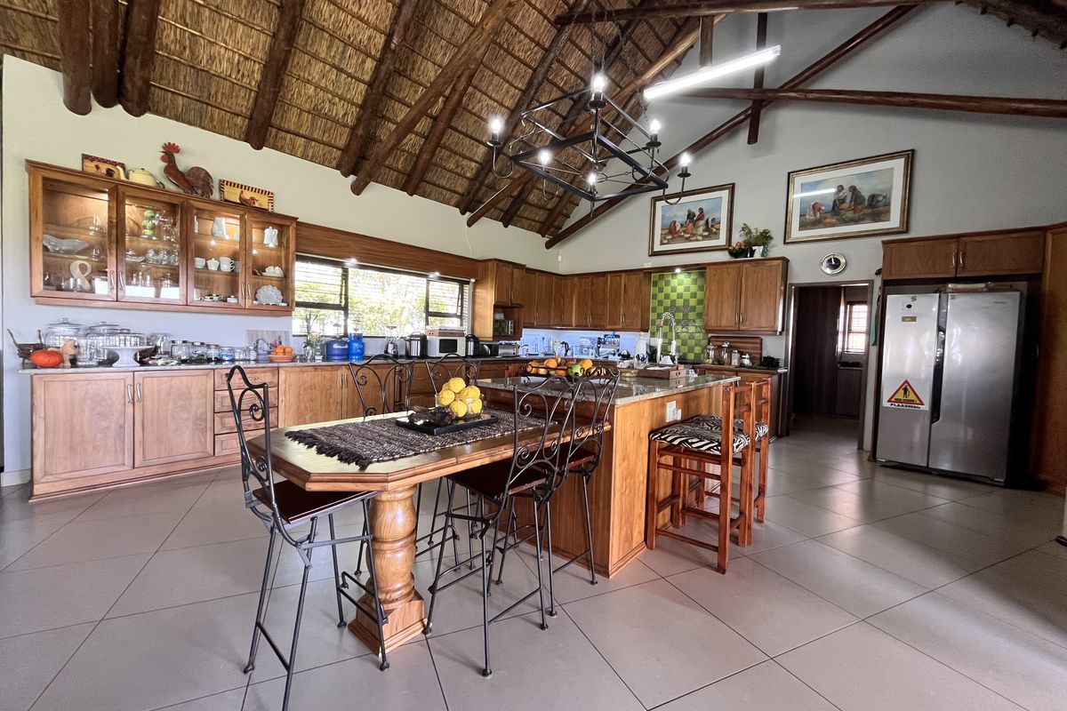 Spacious farmhouse-style kitchen featuring high vaulted thatch ceilings with exposed timber trusses, wooden cabinetry, a central island, and tiled flooring.