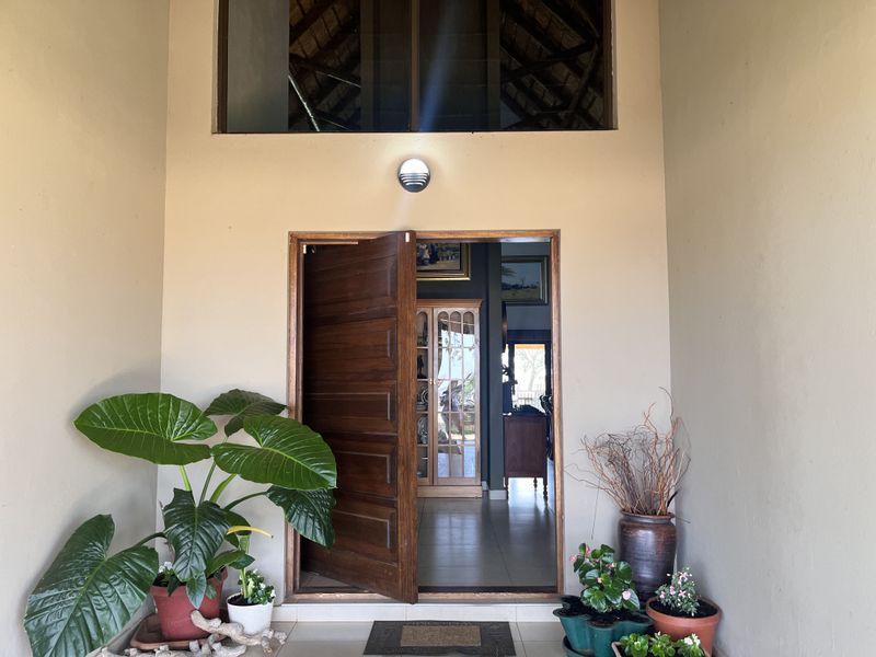 Inviting entrance featuring a solid timber door, double-volume ceiling with exposed thatch detailing, and a welcoming covered porch area.