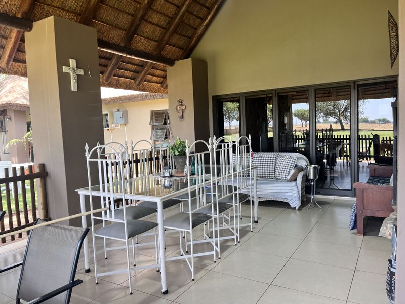 A spacious covered patio featuring a thatched roof, tiled flooring, and large sliding glass doors that provide seamless access to the interior living space.