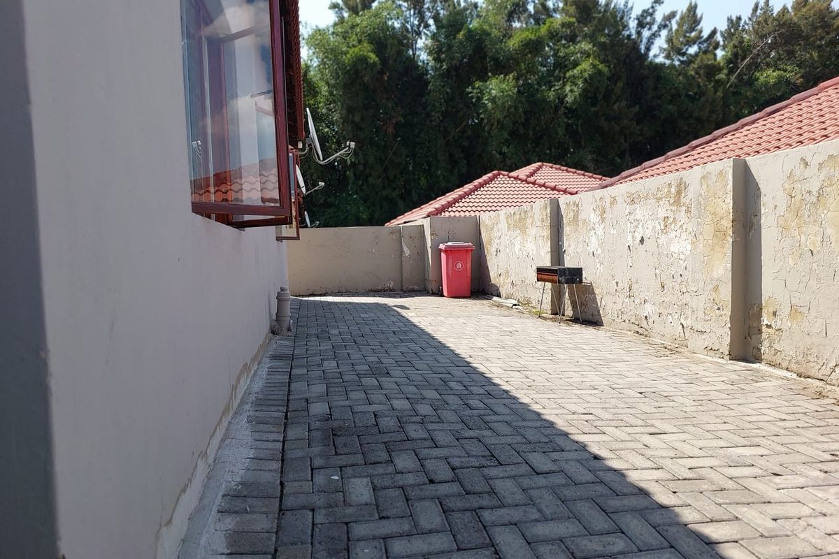 Rear paved patio area featuring a boundary wall with visible weathering and peeling paint, offering a private outdoor space.