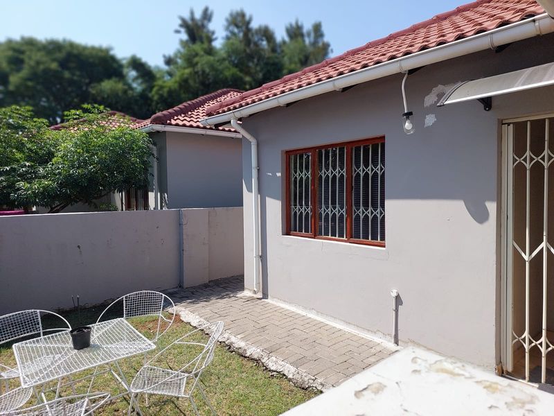 Rear exterior view of the townhouse featuring a small paved patio area, security gates, and a private garden space.