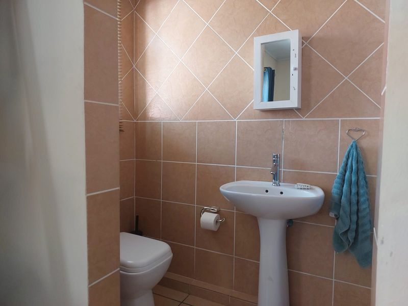 A functional bathroom featuring a pedestal basin, toilet, and wall-mounted medicine cabinet, finished with neutral ceramic wall tiles.