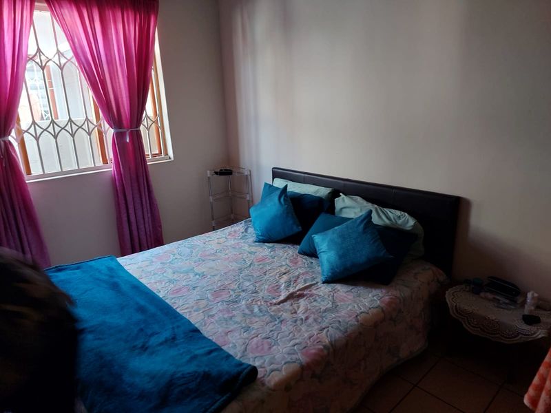 A standard bedroom featuring tiled flooring and a window fitted with a security gate.