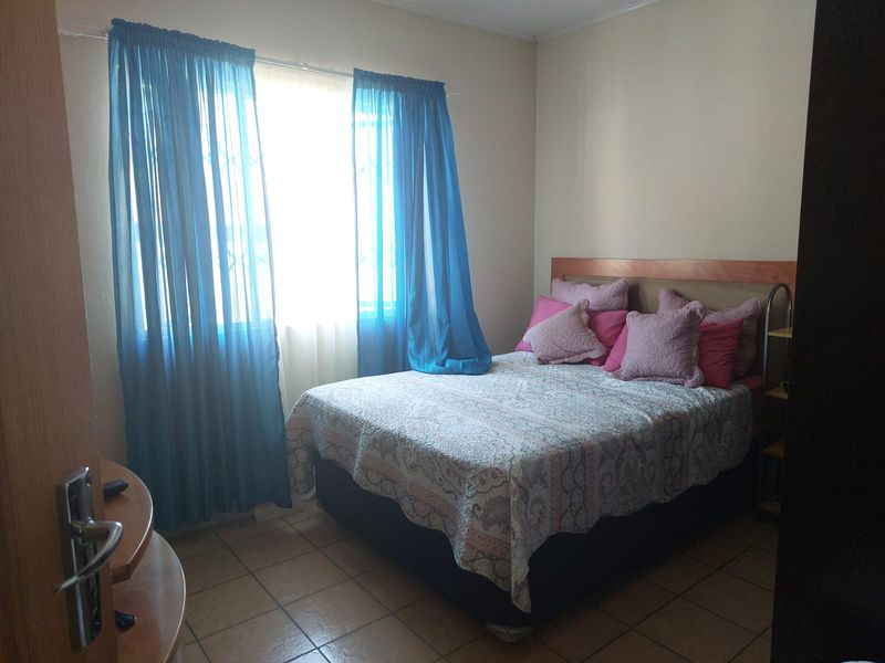 A standard bedroom featuring tiled flooring and a window fitted with a security gate, providing natural light.