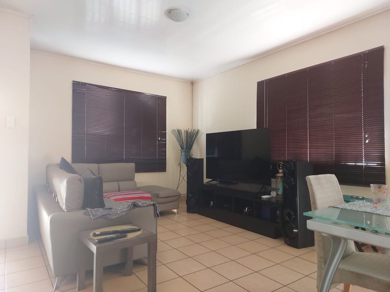 A functional living room featuring tiled flooring and dark venetian blinds, providing a neutral base for interior updates.