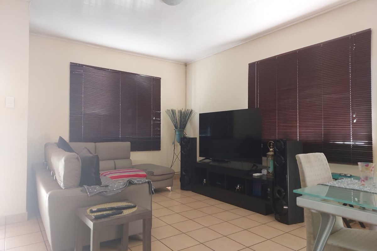 A functional living room featuring tiled flooring and dark venetian blinds, providing a neutral base for interior updates.