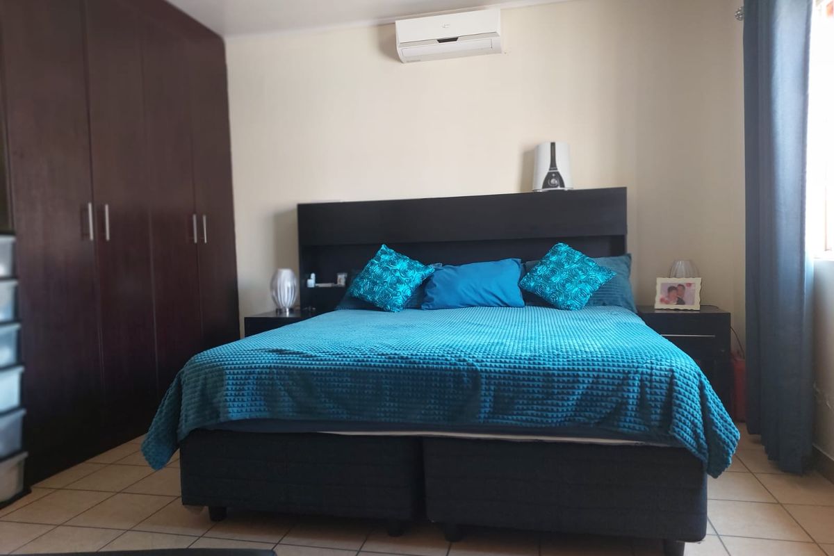 A bedroom featuring tiled flooring, built-in cupboards, and a wall-mounted split-system air conditioner.