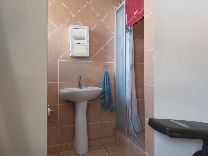 A functional bathroom featuring a pedestal basin, tiled walls, and a shower enclosure with a glass door.