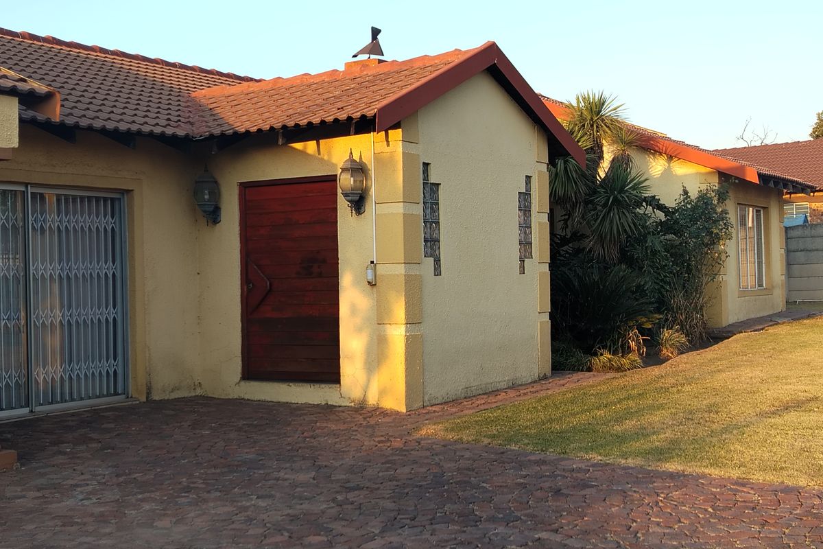 Rear exterior view of the house featuring a tiled roof, brick paved patio area, and security gate access.