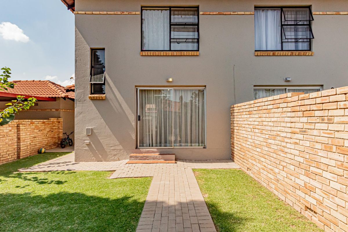 Rear view of the townhouse featuring a private garden, paved walkway, and sliding door access to the main living area.