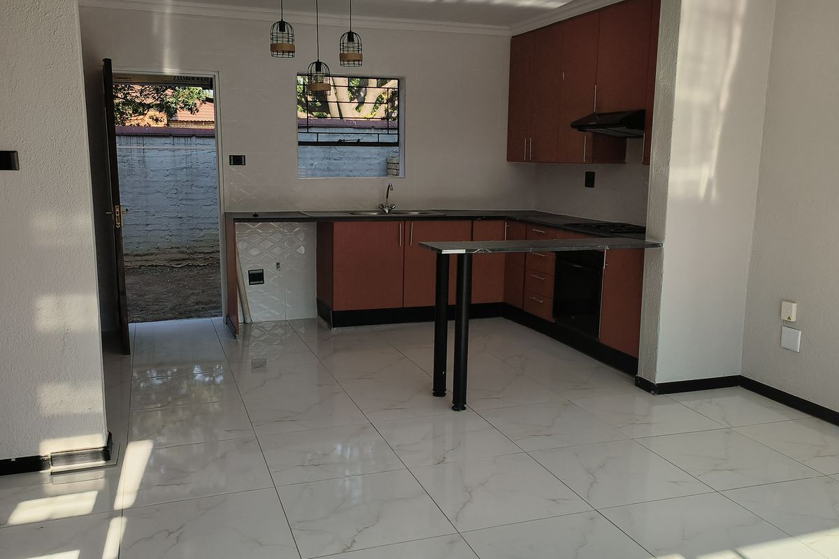 An open-plan kitchen featuring wood-tone cabinetry, a breakfast bar, and modern white marble-look floor tiles, with direct access to the rear exterior.