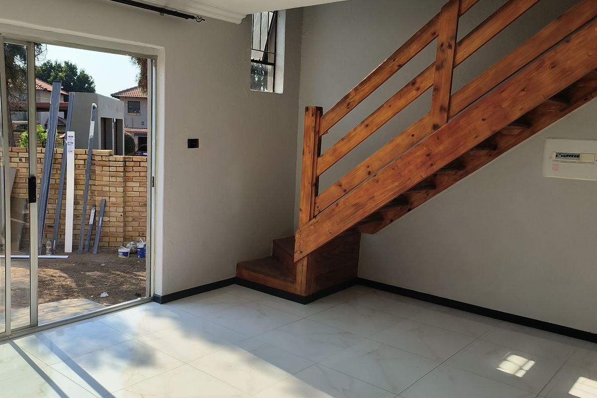 An empty living area featuring modern tiled flooring, a wooden staircase, and a sliding glass door providing access to the exterior.