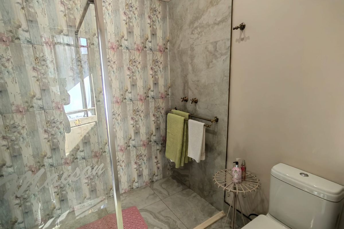 A bathroom featuring a glass-enclosed shower with decorative floral wall tiles, grey floor tiles, and a standard toilet.