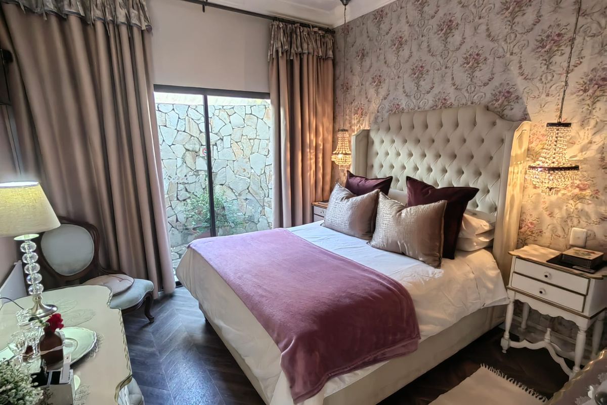 A well-appointed bedroom featuring herringbone flooring, elegant floral wallpaper, and a sliding glass door that opens to a private stone-walled courtyard.