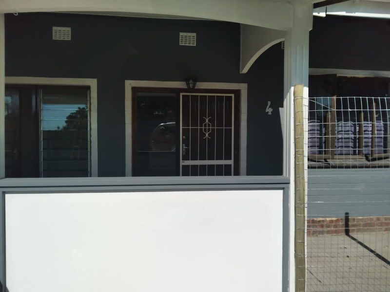 Front entrance of the cottage featuring a covered porch, security gate, and louvered windows with dark grey exterior wall finish.