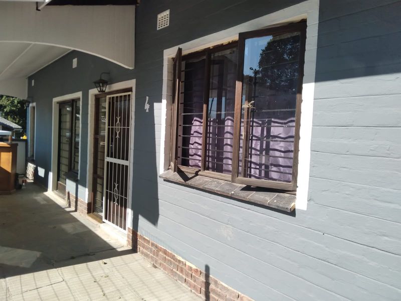 Front exterior view of the cottage featuring a covered walkway, security gates, and dark grey painted brick facade with security bars on windows.