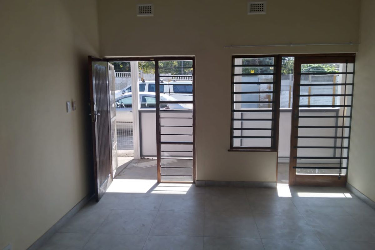 An empty, light-filled living area featuring neutral tiled flooring and direct access to the exterior through secure glass panel doors.