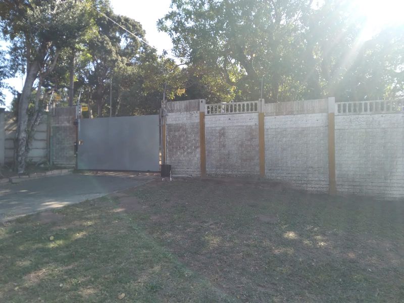 Front exterior view of the property featuring a perimeter wall with electric fencing and a solid security gate leading to the driveway.