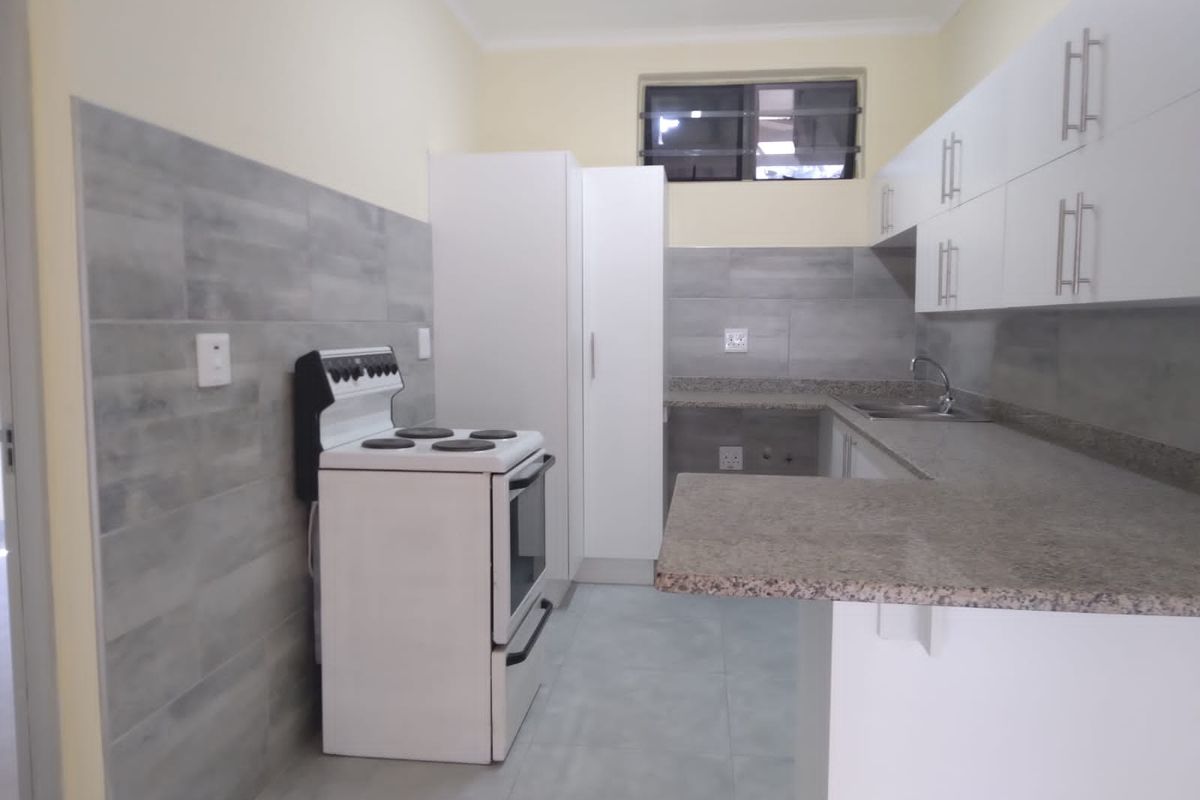 A clean, modern kitchen featuring white cabinetry, granite countertops, grey tiled backsplash, and a freestanding stove in a well-maintained, neutral space.