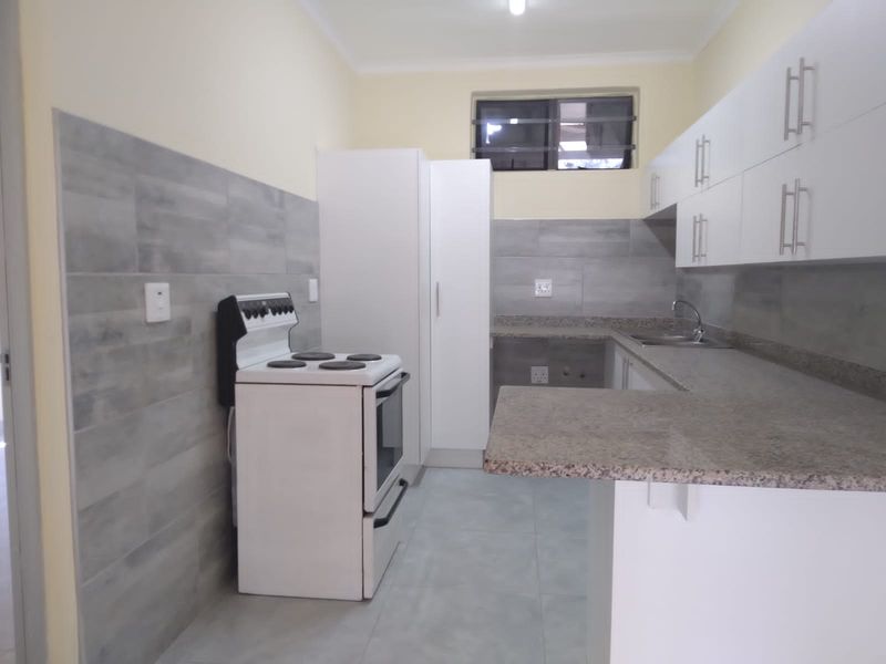 A clean, modern kitchen featuring white cabinetry, granite countertops, grey tiled backsplash, and a freestanding stove in a well-maintained, neutral space.