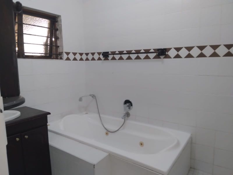 A functional bathroom featuring a built-in bathtub with shower mixer, vanity cabinet, and tiled walls with a decorative border.