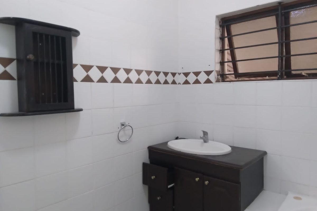 A functional bathroom featuring a vanity cabinet with basin, tiled walls, and a window with security bars, requiring minor cosmetic updates.